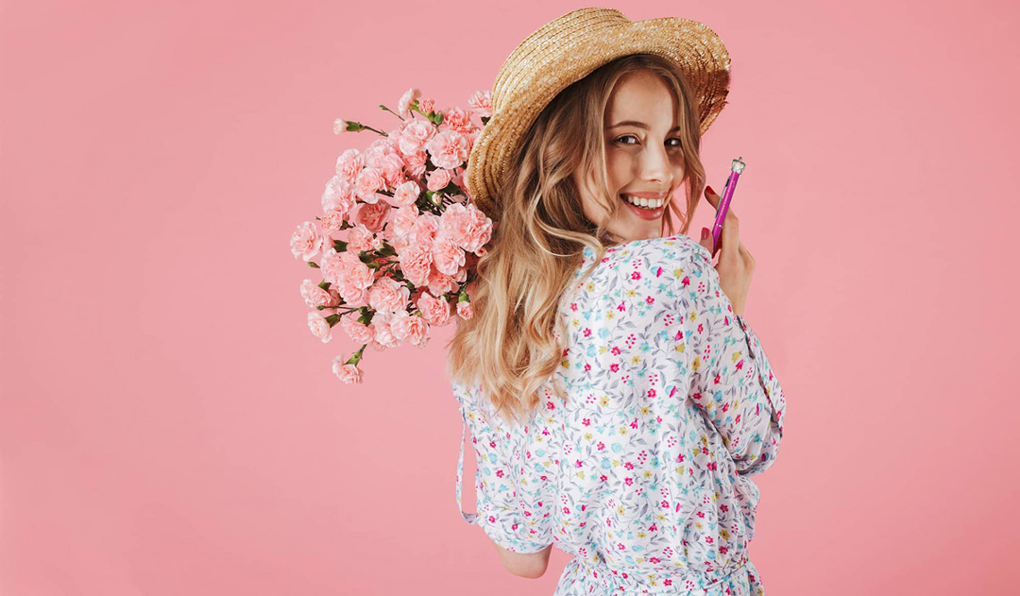 Frau mit Blumen und Strohhut hält den rosa Chica Linda Bonita Kugelschreiber mit Krone in der Hand