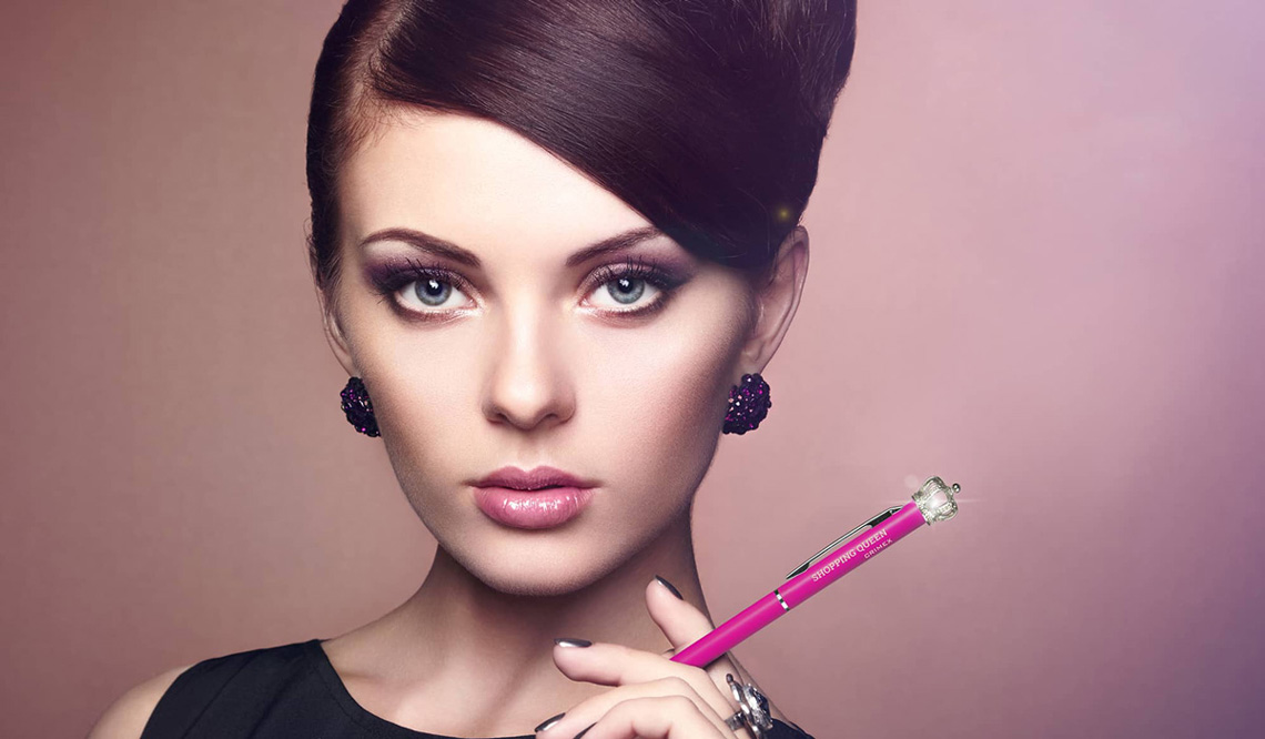 Frau hält rosa Shopping Queen Kugelschreiber mit Krone in der Hand